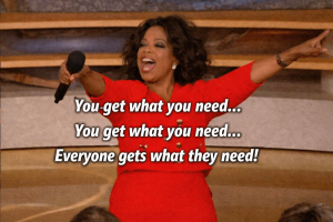 Picture description - Oprah wearing a red skirt suit, looking happy and pointing at the audience with a black microphone in her hand